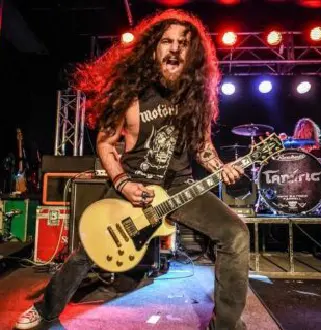 A man with long hair and a beard playing guitar.