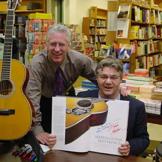 Two men are holding a book with an image of a guitar.