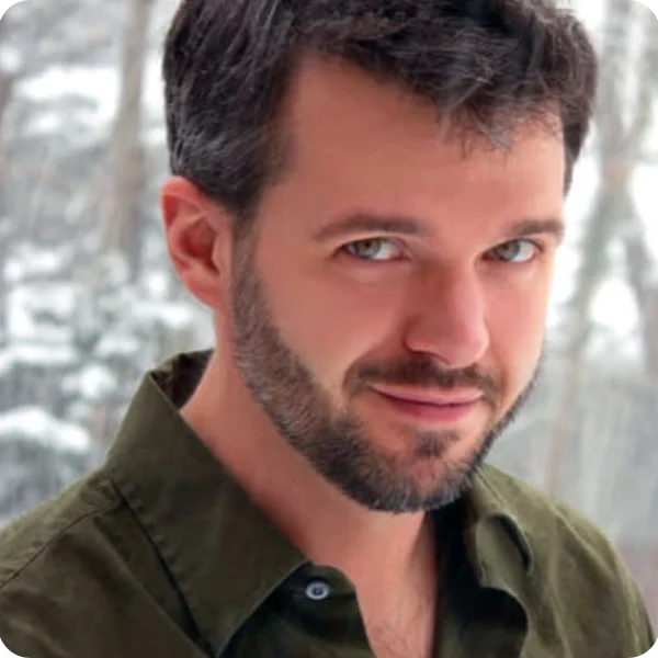 A man with beard and green shirt in front of trees.